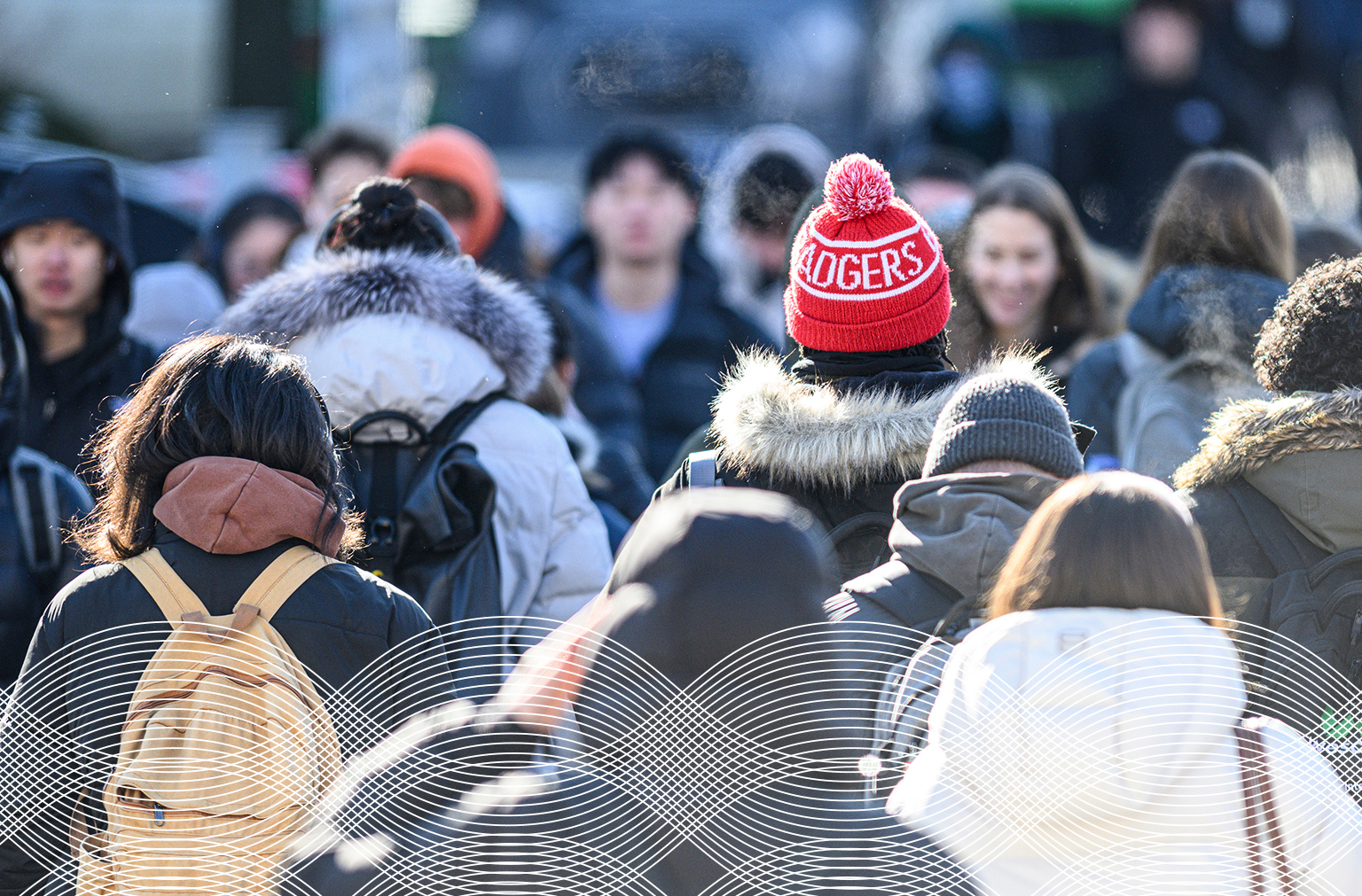 Group of people walking outdoors in winter, wearing coats and hats, with white wavy graphic lines along the bottom of the image.