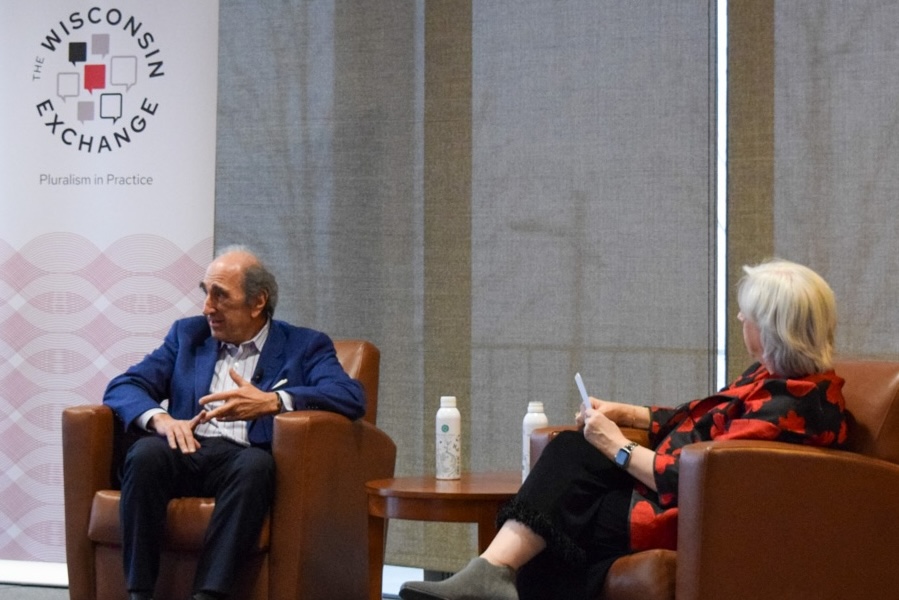 Two people sit in chairs at the head of a room during a discussion.